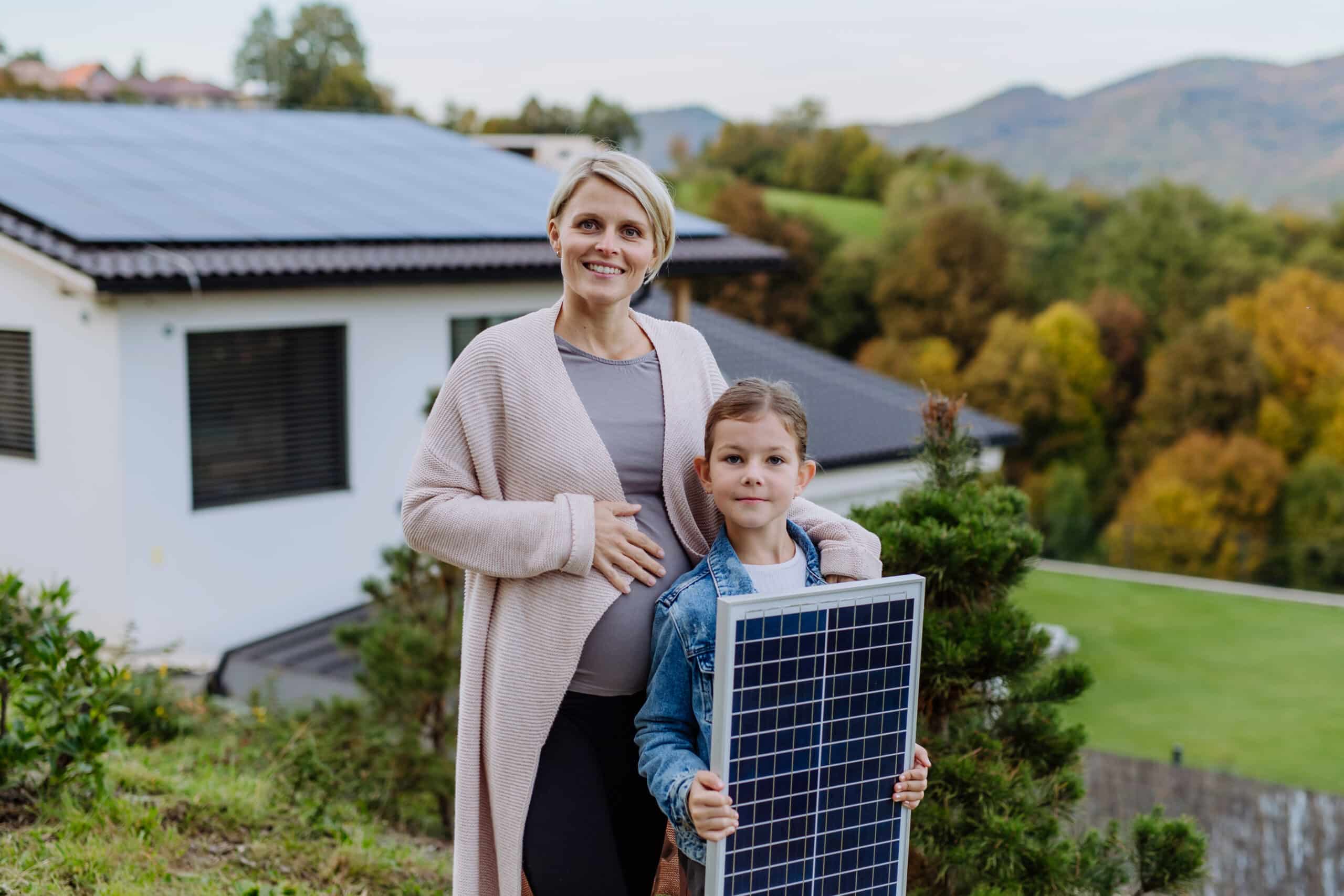 mother with her little daughter near their house with solar panels. alternative energy, saving resources and sustainable lifestyle concept.