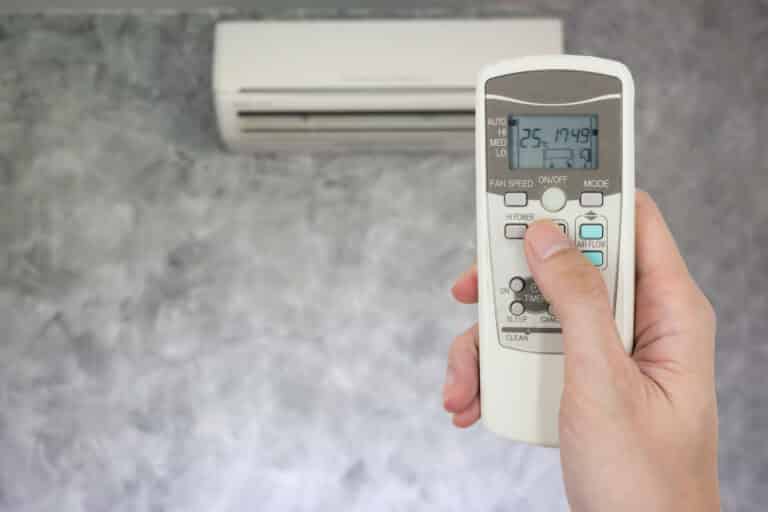 hand holding remote in front of air conditioner.