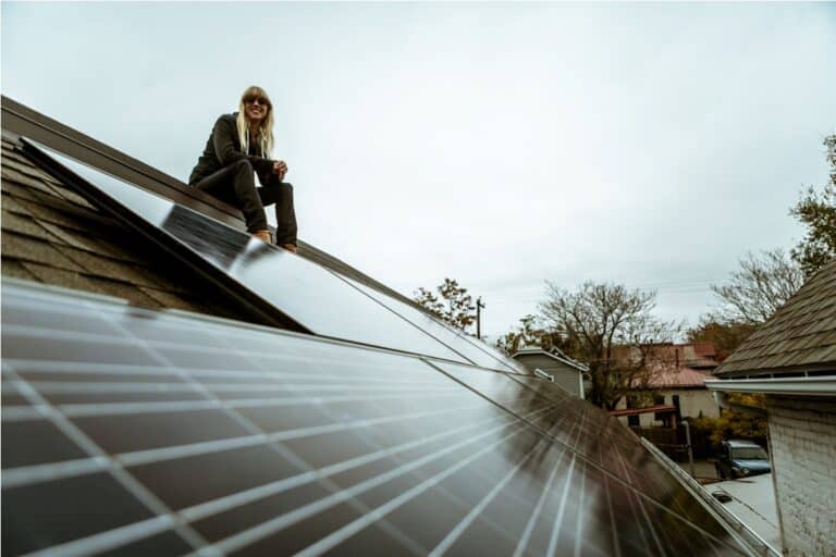 portrait of mid adult woman sitting on newly solar paneled house roof