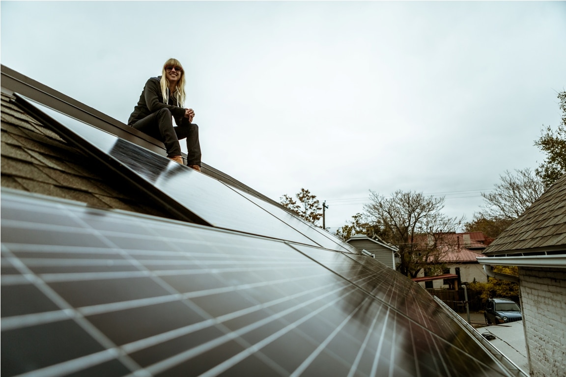 portrait of mid adult woman sitting on newly solar paneled house roof