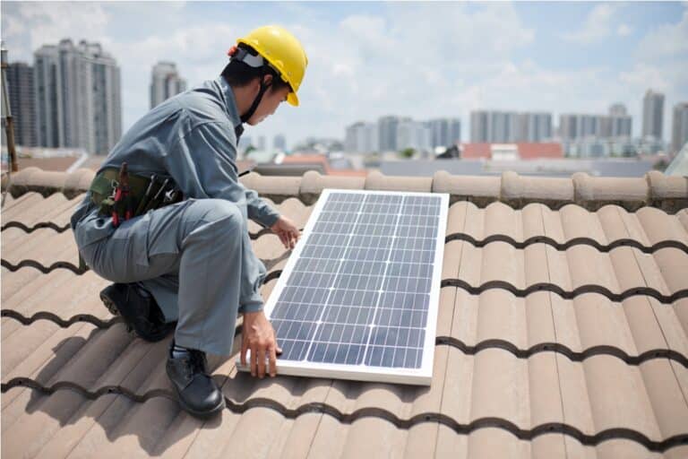 cropped image of worker installing solar panels on roof of residential building