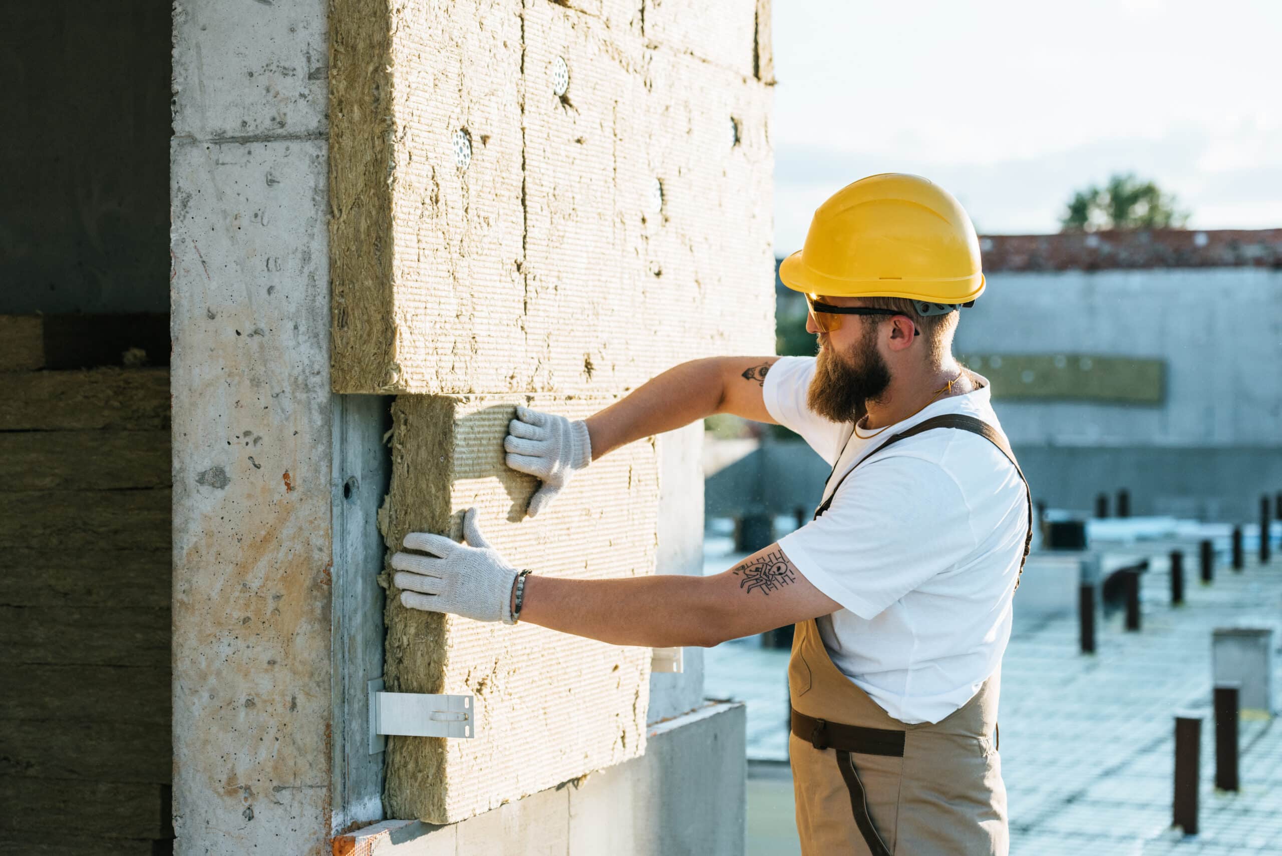 builder in protective helmet and googles doing insulation of wall at construction site