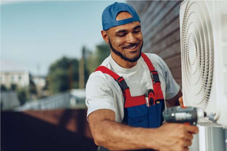 repairman in uniform installing the outside unit of air conditioner